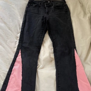 Unika jeans med rosa detaljer - Svarta jeans med breda utsvängda ben och rosa tyginslag längs sidorna samt rosa bakficka. Har sytr om dem själv och dem är perfekt för dig som vill sticka ut med en cool och färgglad look.