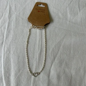Silverfärgat halsband med hjärta - Handgjort halsband i silverfärg med en tunn kedja och ett litet hjärta som hänge. Perfekt för dig som gillar enkla och stilrena smycken. Passar till många olika stilar och är lätt att matcha med andra accessoarer.