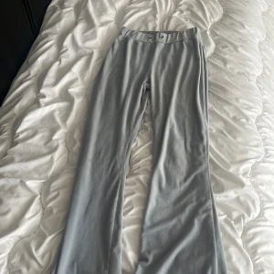 Ljusgrå bootcut byxor från Gina Tricot - Säljer ett par ljusblåa bootcut byxor från Gina Tricot i mjukt material. Byxorna har låg midja, vida ben och snygga metallringar som detalj i midjan. Perfekta för dig som gillar en trendig och bekväm stil.