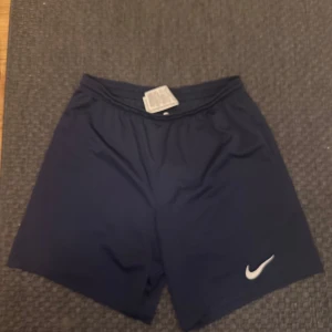 Svarta träningsshorts från Nike - Snygga svarta träningsshorts från Nike med klassisk vit logga på ena benet. Shortsen har elastisk midja och är perfekta för gymmet eller löprundan. Lätta och bekväma med en stilren look. XL men sitter L/M