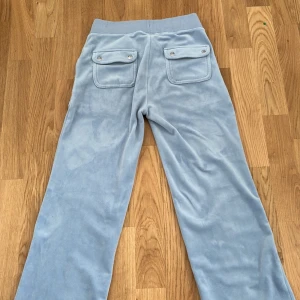 Ljusblå mjukisbyxor med snörning (juciy byxor) - Säljer ett par ljusblå mjukisbyxor med bred resår i midjan och snörning med silverdetaljer. Byxorna har stora fickor fram och bakfickor med lock och knappar. Mjukt material och relaxed passform.