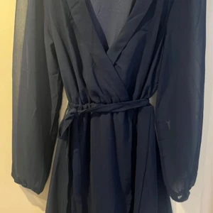 Mörkblå omlottklänning från NLY Trend stl 38 - Säljer en mörkblå omlottklänning från NLY Trend i storlek 38. Klänningen har långa ärmar, knytband i midjan och en v-ringad omlottfront. Perfekt för dig som gillar en klassisk och stilren look.