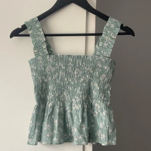 Uniqlo linne smock topp - Blågrönt mönstrat linne/topp med smock-detaljer från Uniqlo. Storlek S. Peplum-passform. Helt nytt, lapp kvar.