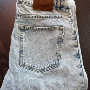 Vintageblå jeans från Woodbird - Säljer ett par vintageblå jeans från Woodbird, modell Leroy Train Jeans. Jeansen har klassisk femficksdesign, normal passform och är tillverkade i ekologisk bomull. Snyggt läderpatch bak i midjan och ljus tvättad denim. OBS! Fläck på ett knä