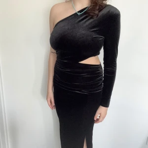 Svart sammetsklänning med oneshoulder och slits - Säljer en svart långklänning i sammet med oneshoulder-design och lång ärm. Klänningen har en snygg cut-out vid midjan och en slits framtill. 