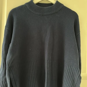 Mörkblå stickad tröja från ONLY - Säljer en mörkblå stickad tröja från ONLY med ribbade partier nedtill och vid ärmsluten. Tröjan har hög hals och långa ärmar, perfekt för kyligare dagar. Enkel och stilren design som passar till mycket.