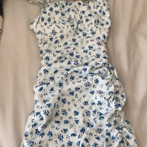 Vit blommig kortklänning med blått mönster - Säljer denna eftersom jag aldrig använt den förutom en gång. Den är från shein och i storlek Xs.Det är en söt vit kortklänning med blått blommigt mönster. Klänningen har smala axelband och en tight passform som framhäver figuren. Perfekt för varma dagar och somriga tillfällen.