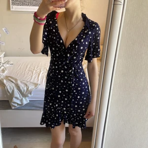 Mörkblå omlottklänning med stjärnmönster från Boohoo - 50kr passar XXS-S (möjligen M)Supersöt mörkblå omlottklänning från Boohoo med vita stjärnor över hela tyget. Klänningen har korta ärmar, volangkant nertill och knyt i midjan. Perfekt för dig som gillar en lekfull och trendig stil!