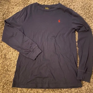 Mörkblå långärmad tröja från Polo Ralph Lauren - Säljer en mörkblå långärmad tröja från Polo Ralph Lauren med klassisk röd broderad logga på bröstet. Tröjan är i bomull och har en enkel, stilren design med rund hals. Perfekt för en avslappnad och snygg look. Tröjan är i storleken L (14-16) men sitter som en XS-S.👍🟦🟥