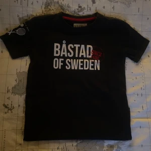 Svart t-shirt från Båstad - Svart t-shirt från Båstad med stort vitt tryck 'Båstad of Sweden' och röd detalj 'Since 1450' på bröstet. Klassisk rund halsringning med röd insida. 