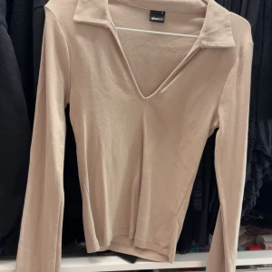 Beige långärmad topp med krage från Gina Tricot - Säljer en beige långärmad topp från Gina Tricot med v-ringning och krage. Tunn och mjuk i materialet, perfekt för lager-på-lager eller som den är. Enkel och stilren design som passar till mycket.