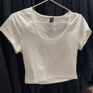 Vit croppad t-shirt från T - Säljer en enkel och stilren vit croppad t-shirt. T-shirten har korta ärmar och en rund, djup urringning. Perfekt att matcha med jeans eller kjol för en avslappnad look.