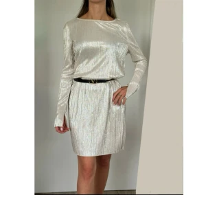 Skimrande klänning från Gina Tricot i XS - Säljer en skimrande klänning från Gina Tricot i en elegant guld/champagnefärgad med skimrande effekt. Passar S-XXS. Användes på en enda fest. Den passar lika bra till vardags som till fest. Kan användas med eller utan skärp.  OBS! Skärp ingår ej!  Personen på bilden är ca 160 cm lång och har XXS i storlek .