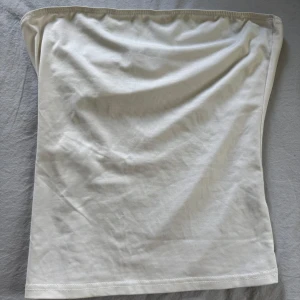 Vit tubtopp - En enkel och stilren vit tubtopp i mjukt material. Perfekt att matcha med jeans eller kjol för en clean look. Toppen är axelbandslös och har en rak passform.