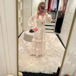 Vit långklänning i spets med volanger - Säljer en romantisk vit långklänning i spets med volangdetaljer och lång ärm. Klänningen har v-ringning, markerad midja och en liten öppning framtill. Perfekt för sommarens tillfällen!