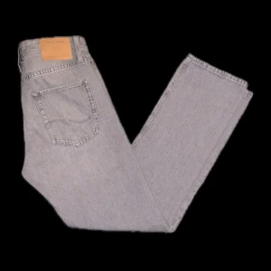 Grå jeans från Jack & Jones - Säljer ett par grå jeans från Jack & Jones med klassisk femficksdesign och rak passform. Byxorna har normal midja och är tillverkade i ett mjukt jeanstyg. Perfekta för dig som gillar en stilren och enkel look.