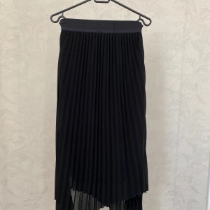 Svart plisserad kjol  - Säljer en svart plisserad kjol med snygg asymmetrisk fåll. 