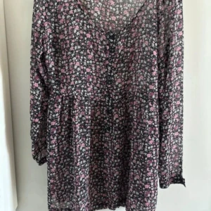 Blommig långärmad blus - Söt blus med småblommigt mönster i rosa och vitt på svart botten. Klänningen har v-ringning, knappar framtill och långa ärmar. 