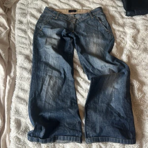 Blå jeansbyxor med vida ben från Vila - Säljer ett par blå jeansbyxor från Vila med breda ben och klassisk femficksdesign. Byxorna har normal passform och är tillverkade i denim med snygga slitningar framtill. Perfekta för en avslappnad och trendig look. Den är väldigt låg midjad även om det inte ser så på bilen men den är det. 