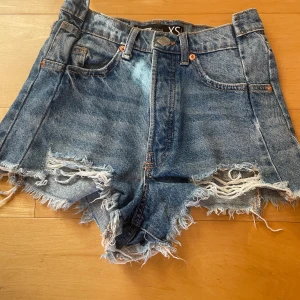 Blå jeansshorts med fransar - Säljer ett par blå jeansshorts med råa, fransiga kanter och slitningar framtill. Perfekta för sommaren och ger en cool, avslappnad look