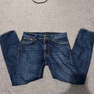 Blå jeans Lean Dean från Nudie Jeans - Säljer ett par klassiska blå jeans från Nudie Jeans, modell Lean Dean. Jeansen har fem fickor, orangea sömmar och är tillverkade i 99% bomull och 1% elastan för lite stretch. Perfekta till vardags med snygg passform.
