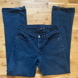 Mörkblå bootcut jeans från Sandco - Mörkblå jeans från Sandco med klassisk femficksdesign och bootcut-ben. Jeansen har normal passform och är tillverkade i ett mjukt denimtyg. Jeansen är dock lite slitna som man kan se på sista bilderna. Men perfekta för dig som gillar en tidlös stil!