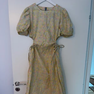 Blommig midilångklänning från Damson Madder - Säljer en romantisk midilångklänning från Damson Madder i ljusa pastellfärger med blommigt mönster. Klänningen har korta puffärmar med resår, knytband i midjan och är tillverkad i 100% ekologisk bomull. Perfekt för sommarens tillfällen!