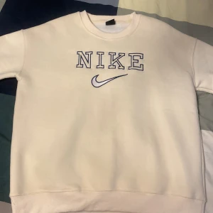 Vit sweatshirt från Nike - Säljer en banan\vit sweatshirts från Nike med broderad logga och text i blått framtill. Tröjan har rund halsringning och långa ärmar. Perfekt för en avslappnad och sportig stil.