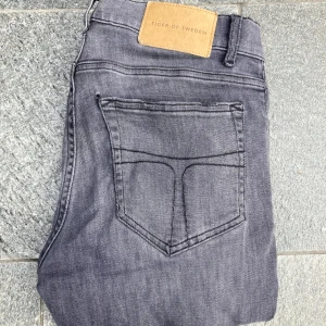 Grå jeans från Tiger of Sweden - Feta grå jeans från Tiger of Sweden i modellen Evolve. Storlek 26 32. Skicket är mycket bra, med original slitningar (se bild 4&5). Nypriset ligger på ungefär 1700kr, mitt pris 375kr, ej hugget i sten. Hör av dig vid frågor eller funderingar. 