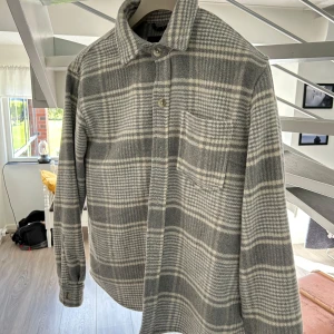 Gråvit rutig overshirt från Pull&Bear - Säljer en stilren grå och vit rutig overshirt från Pull&Bear. Jackan har klassisk krage, knäppning framtill och en bröstficka. Perfekt lager-på-lager-plagg med avslappnad passform och mjukt material.
