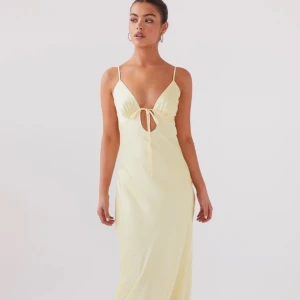 Ljusgul långklänning med knyt och öppen rygg - Säljer en ljusgul långklänning med smala axelband, v-ringning och snygg knytning framtill samt öppen rygg med stor rosett. Helt ny med prislapp, egna bilder kan skickas, vid förfrågan