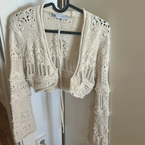 Beige stickad croppad kofta från Zara - Säljer en beige stickad kofta från Zara med vackra virkade detaljer och knytband framtill. Koftan är croppad och har långa ärmar med unikt mönster. Perfekt för lager-på-lager och ger en bohemisk vibe. Trådet knyter man i hålen om man vill 🌸