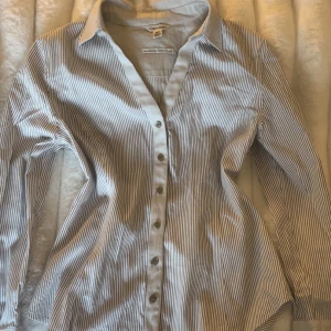 Randig skjorta från Calvin Klein - En klassisk men snygg vit och grå randig skjorta från Calvin Klein. Skjortan har lång ärm, knappar framtill, v-ringning och krage. Använd några gånger.