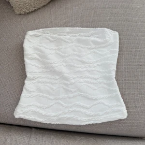 Vit tubtopp med struktur - Säljer en vit tubtopp med vågig struktur i tyget. Toppen är ärmlös och har en lätt stretchig känsla. 