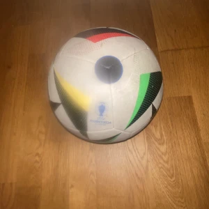 Adidas fotboll EURO2024 - Säljer en officiell Adidas fotboll från EURO2024. Bollen är vit med färgglada detaljer i rött, gult, grönt och svart samt blått EURO2024-märke. Perfekt för fotbollsträning eller matchspel. Klassisk rund form och tillverkad i slitstarkt material.