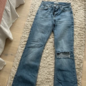 Blå bootcut jeans med hål på knät - Säljer ett par blå bootcut jeans med klassisk femficksdesign och ett stort hål på ena knät. Jeansen har normal passform och är tillverkade i denim. Bra skick knappast använda 