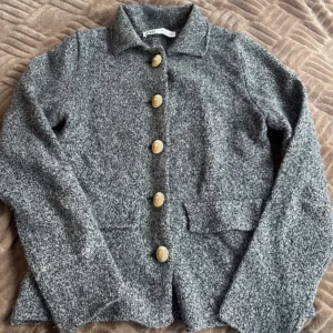 Stickad tröja - Stilren grå tröja från Zara med klassisk krage och stora dekorativa knappar framtill. Jackan har två fickor och lång ärm, perfekt för kyligare dagar.