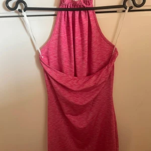 Rosa ärmlös klänning med halterneck - Säljer en snygg rosa klänning med halterneck och draperad rygg. Klänningen är ärmlös och har en tight passform som framhäver figuren. 