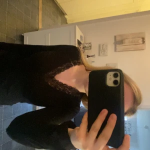 Svart långärmad topp med spets - Säljer en svart långärmad topp med v-ringning och fina spetsdetaljer längs urringningen. Perfekt att styla med jeans eller kjol för en snygg look. Mjuk och skön att ha på sig.