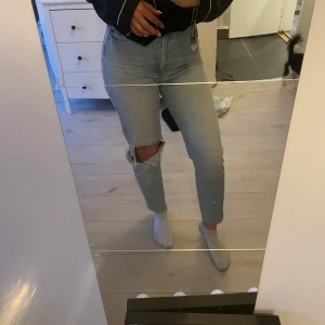 Ljusblå jeans med hål på knät - Säljer ett par ljusblå jeans med hög midja och hål på ena knät. Jeansen har en rak passform och klassiska bakfickor. Perfekta för en avslappnad och trendig look.