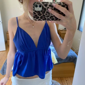 linnetopp från Bik Bok - Säljer en kornblå linnetopp från Bik Bok med smala axelband och djup v-ringning. Toppen har en lös passform nedtill och är tillverkad i ett lätt, syntetiskt material. Perfekt för varma dagar!