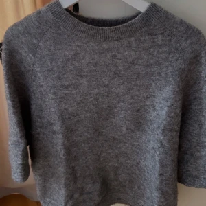 Grå stickad t-shirt  - Mysig grå stickad tröja med rund halsringning och långa ärmar. Perfekt för kyliga dagar och enkel att matcha med olika outfits. Klassisk och stilren design som passar till mycket.