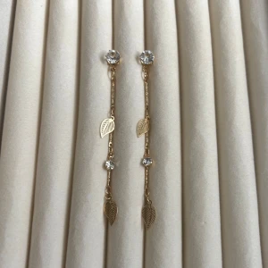 Guldiga hängande örhängen med löv och stenar - Säljer ett par eleganta guldiga örhängen med tunna kedjor, små gnistrande stenar och dekorativa lövdetaljer. Perfekta för att ge en stilren touch till din look.