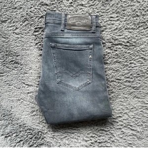 Grå jeansbyxor från Replay - Säljer ett par grå jeansbyxor från Replay med klassisk femficksdesign och raka ben. Byxorna har en snygg tvättad look och Replay-logga på bakfickan samt läderpatch i midjan. Perfekta för dig som gillar stilrena och bekväma jeans. Priset kan diskuteras vid snabb affär 