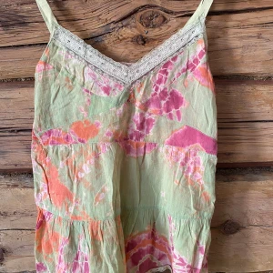Pastellfärgad klänning med spets från Melmelli - Säljer en somrig klänning från Melmelli i pastelliga toner av grönt, rosa och orange. Klänningen har v-ringning med spetsdetaljer och axelband. Mönstret är batik-inspirerat och tyget känns lätt och luftigt.