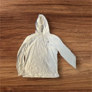 Vit hoodie från Polo Ralph Lauren - Säljer en klassisk vit hoodie från Polo Ralph Lauren. Tröjan har huva och lång ärm, tillverkad i 100% bomull. Liten broderad logga på bröstet. Perfekt för en avslappnad och stilren look.