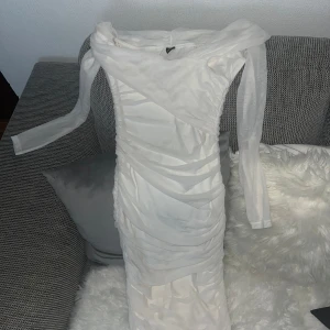 Vit långärmad klänning från SHEIN - Säljer en vit långärmad klänning från SHEIN i storlek XS. Klänningen har en figurnära passform med draperade detaljer och är tillverkad i ett tunt, lätt material. Perfekt för dig som vill ha en stilren och elegant look.