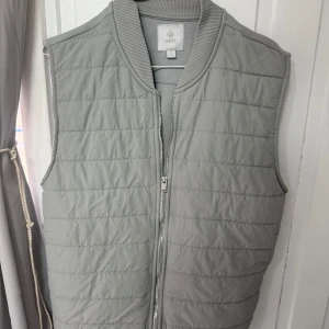 Ljusgrå väst från Next - Snygg ljusgrå quiltad väst från Next med dragkedja framtill och ribbad krage. Perfekt att bära över en hoodie eller tröja för extra värme. Enkel och stilren design som passar till många outfits. Hör av er vid frågor😁