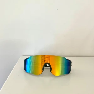 Sportiga solglasögon - Snygga sportglasögon med stora, spegelblanka linser i gult och grönt. Bågarna är svarta och modellen är kantig och modern, perfekt för träning utomhus🏃‍♂️‍➡️ Linsen är bred och ger bra täckning mot solen☀️