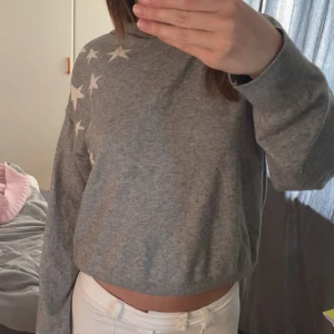 Grå hoodie med stjärnor - Säljer en grå hoodie med vita stjärnor på axel och rygg. Mjuk och skön att bära. Köpt på Gina för 300 säljs inte längre användts 2-3 gånger.